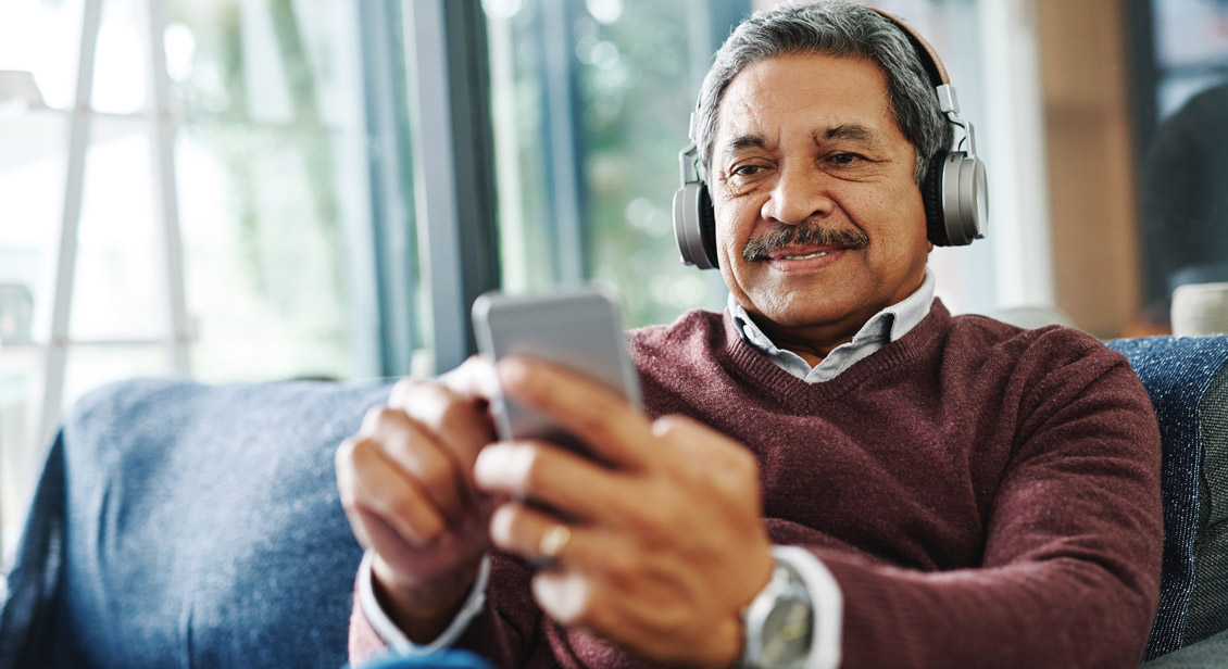 Mature man on couch listening to a podcast on his smartphone
