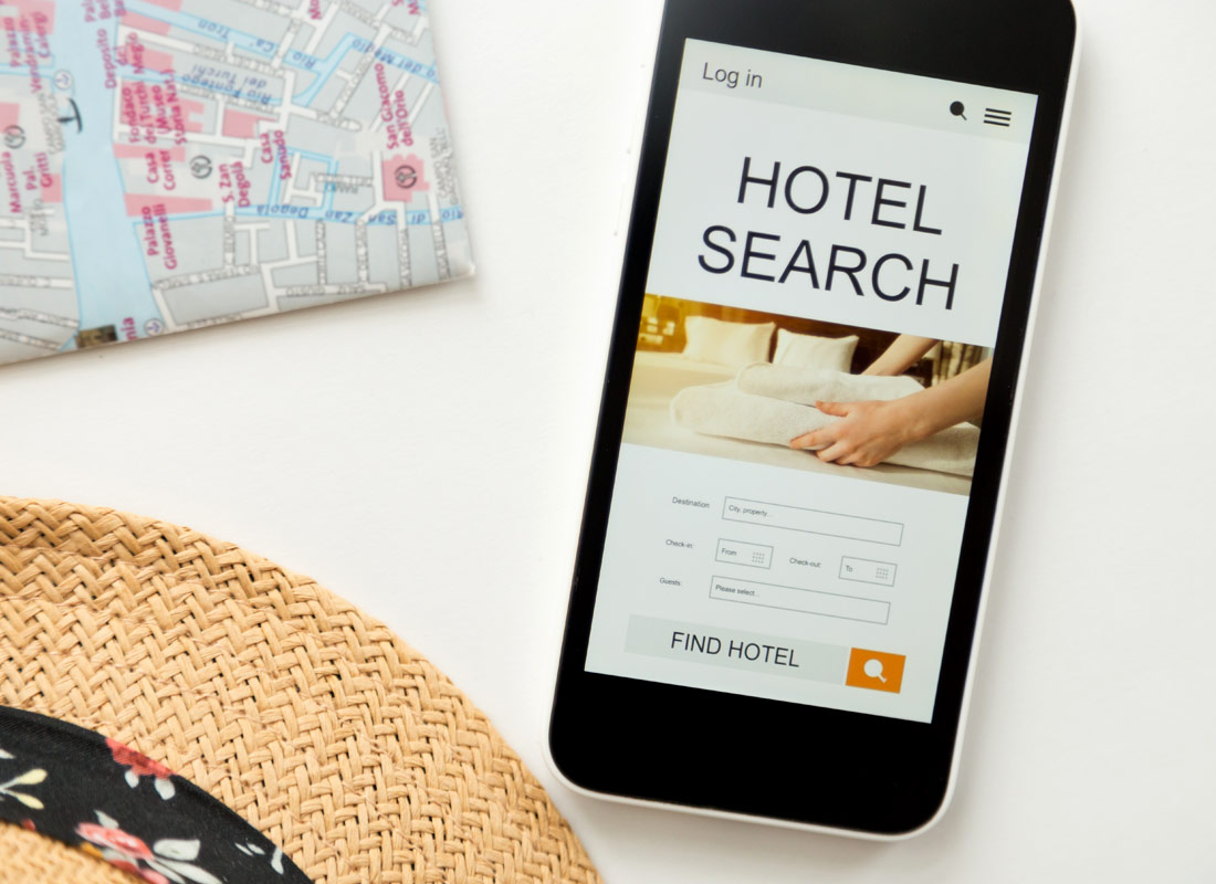 Holiday preparation is happening with a map, a hat and a hotel search on a mobile phone