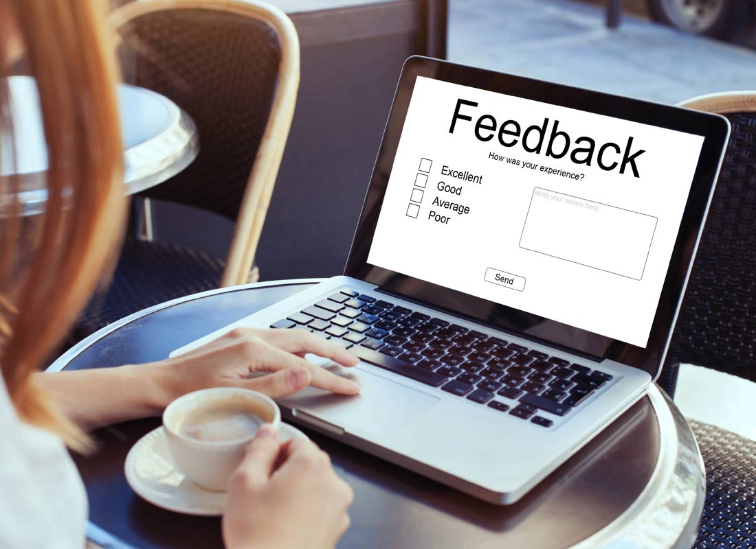 A woman sits at a cafe with her laptop and a coffee with an online feedback form on the screen