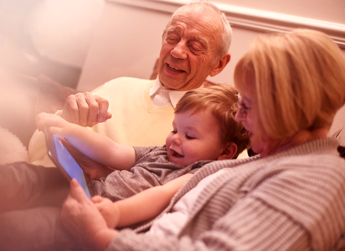 Grandparents and grandchild all sit together enjoying what they are watching on their tablet