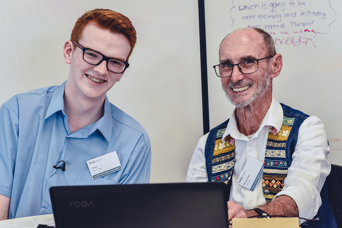 Male teenage student assits senior male using laptop