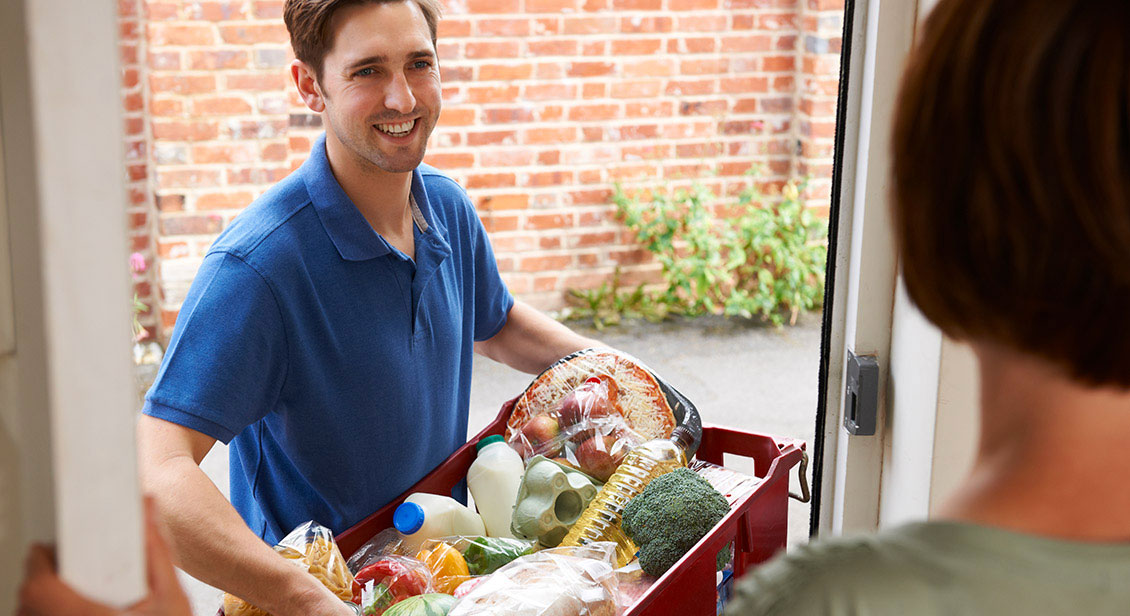 A young man delivers fresh groceries to the home of an older female.