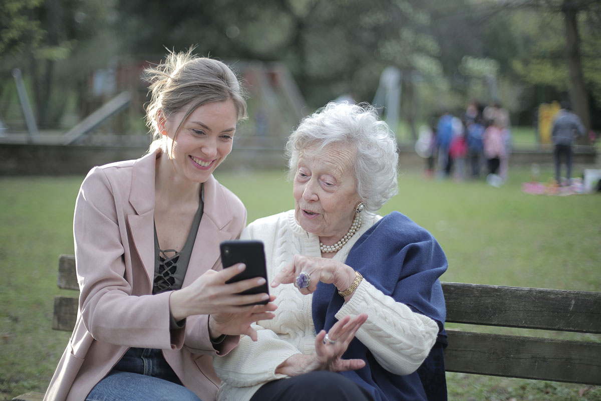 Two ladies sitting on a park bench looking satisfied as they read smart phone