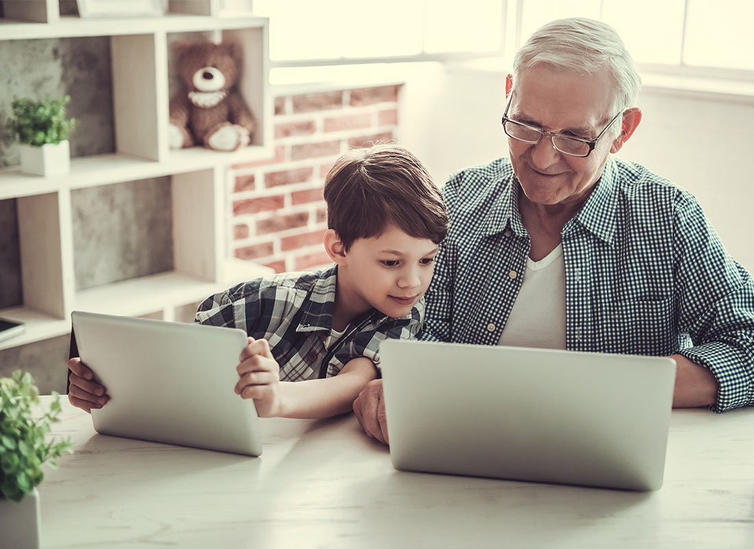 A grandfather and child sharing a tablet and laptop computer together