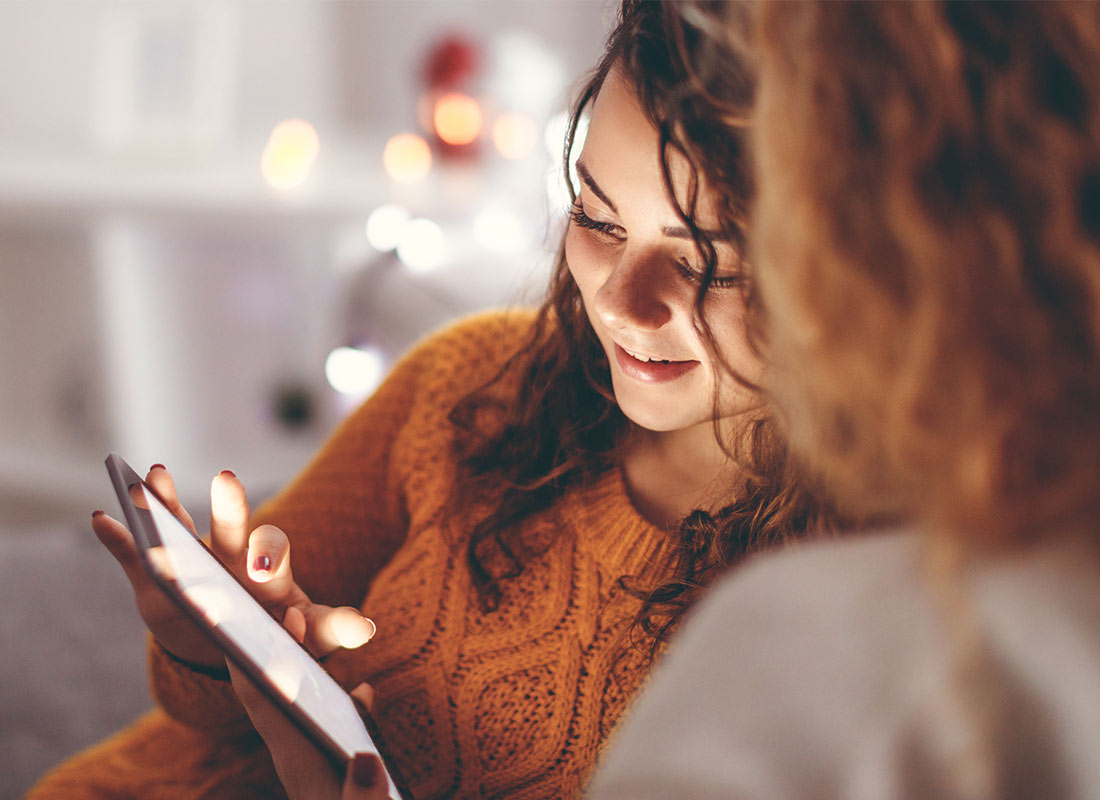 A teenage girl and a woman sitting together looking at something on a tablet at home.
