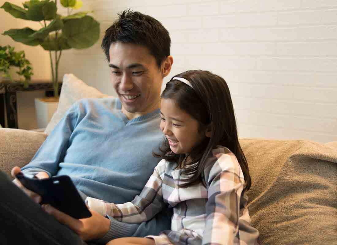 A man and his daughter laughing at something on a smartphone.