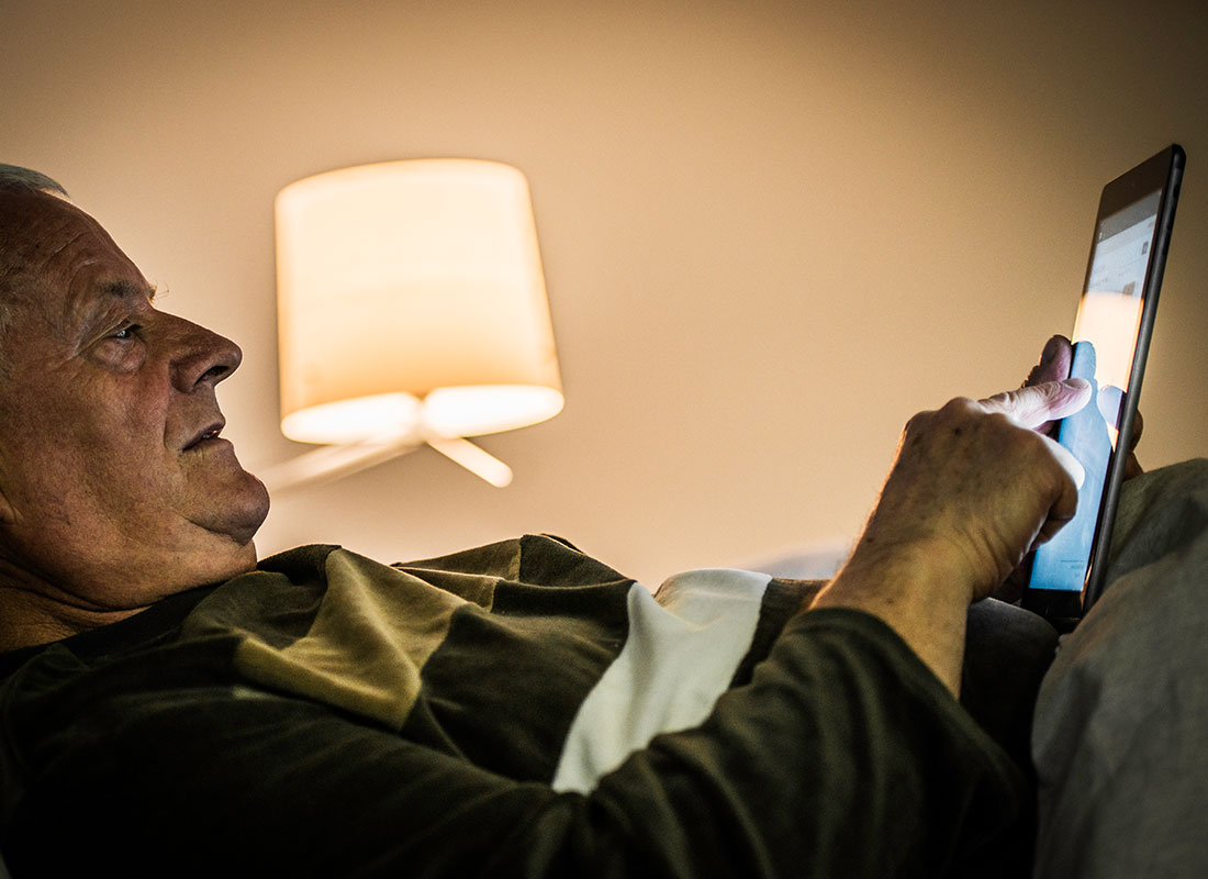 An older man relaxing on his sofa and watching the news on his tablet.