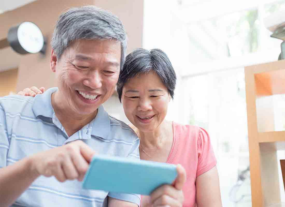An older Asian couple laughing about something on the internet on a smartphone.