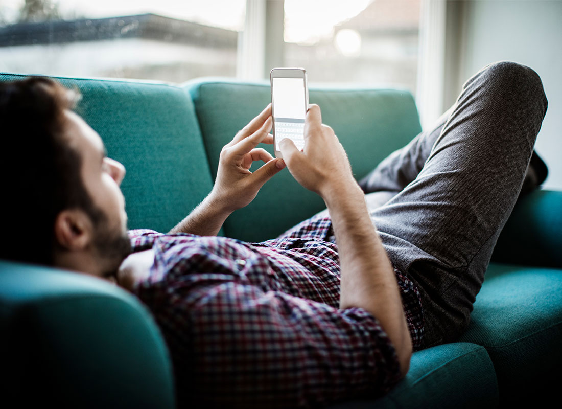 A man relaxing on his sofa using his mobile phone and his home Wi-Fi internet connection to browse the internet.