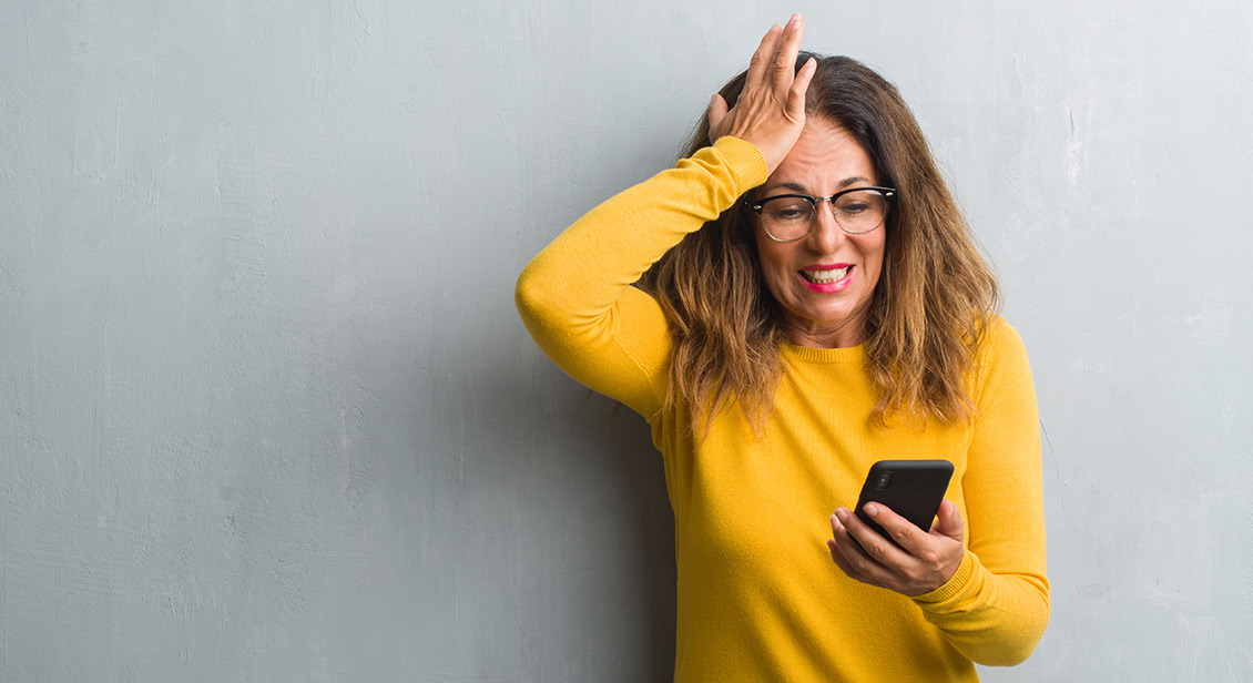 middle aged woman in orange jumper with concerned look on her face viewing her mobile phone