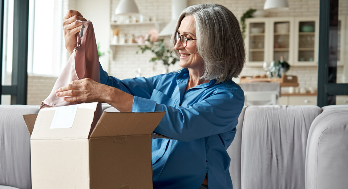 Woman of retirement age opening a package and viewing clothing she has purchased from an online shop 