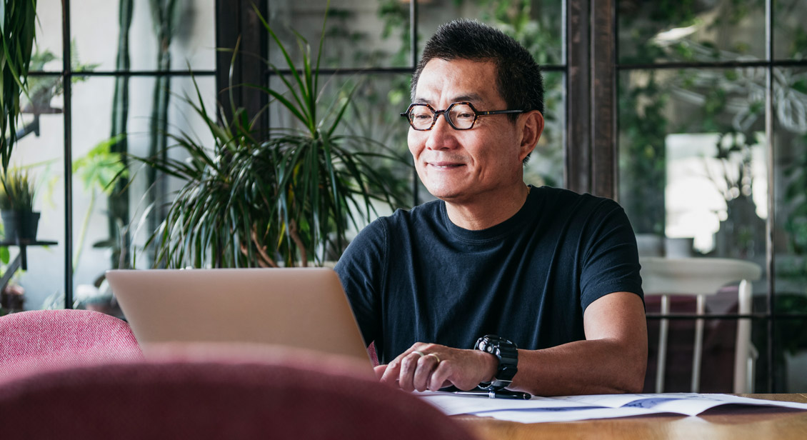 Asian man with glasses sitting at his home desk on a laptop 