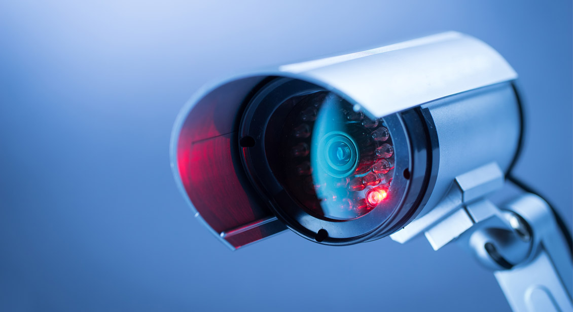 A wall mounted CCTV with a glowing red LED light indicating active recording.