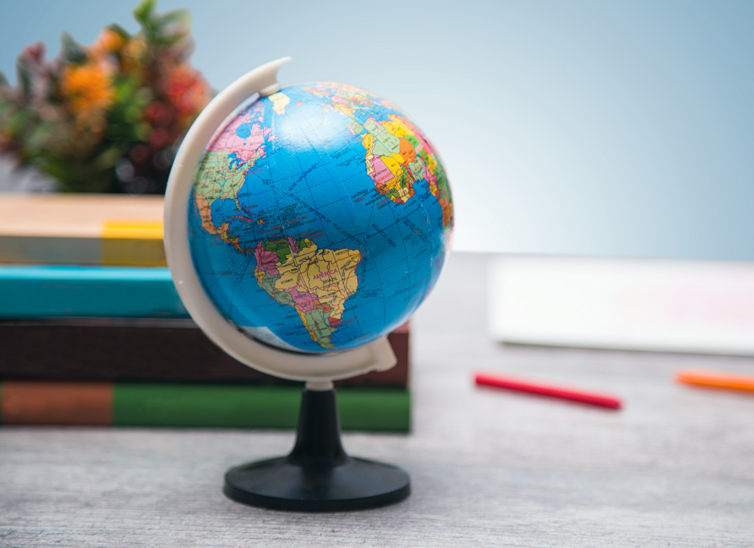 A small globe on a table with books and pencils in the background.