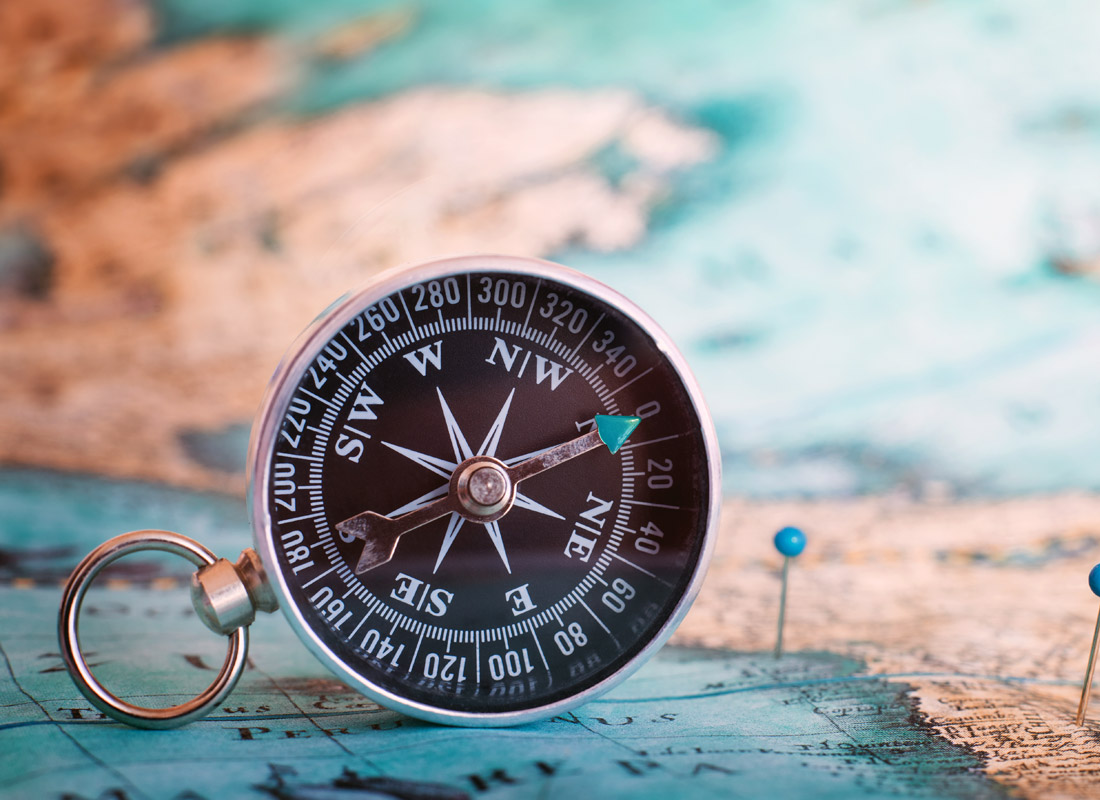 A photograph of a compass leaning on a map with some pins in it.